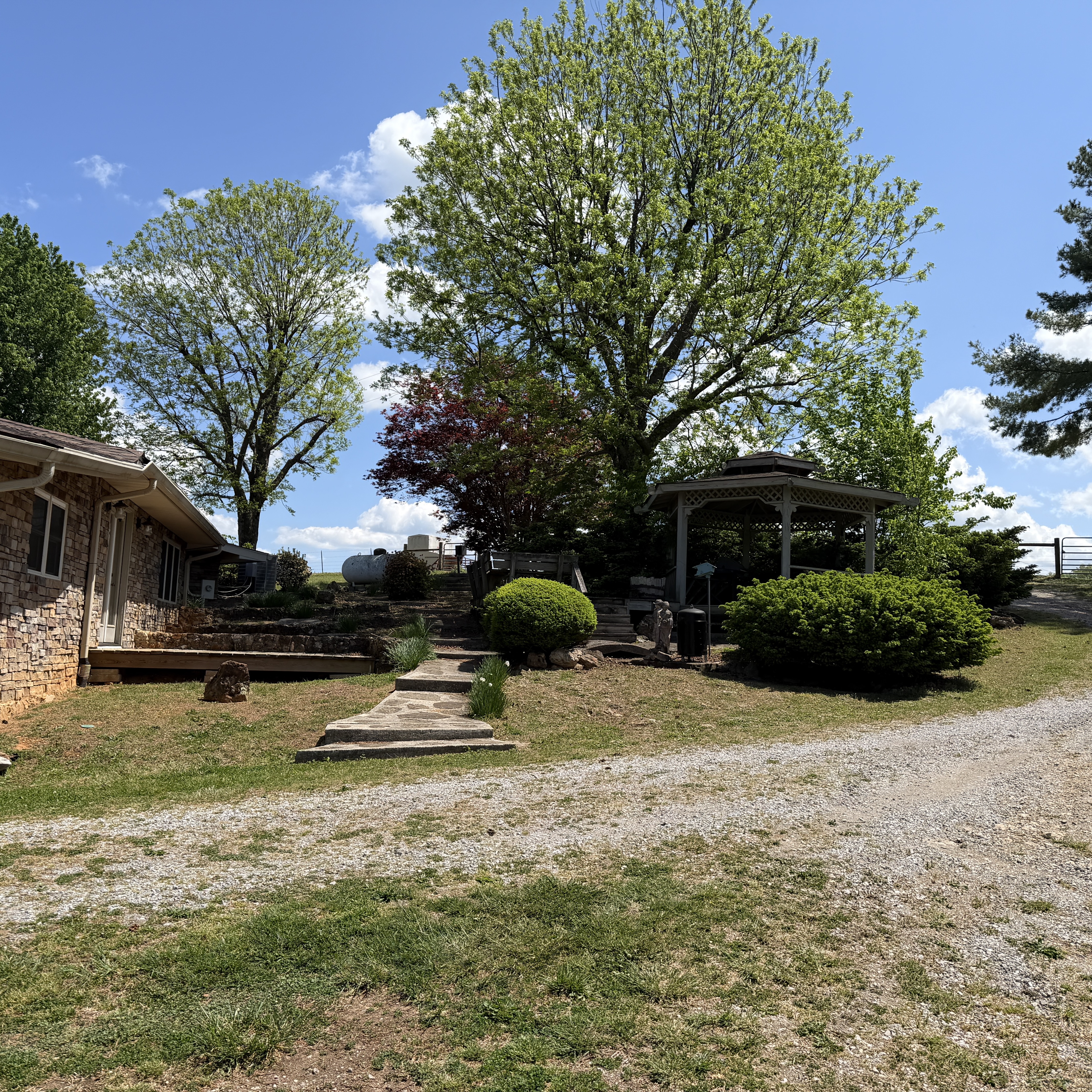 Front of stone home with mature trees and landscaping