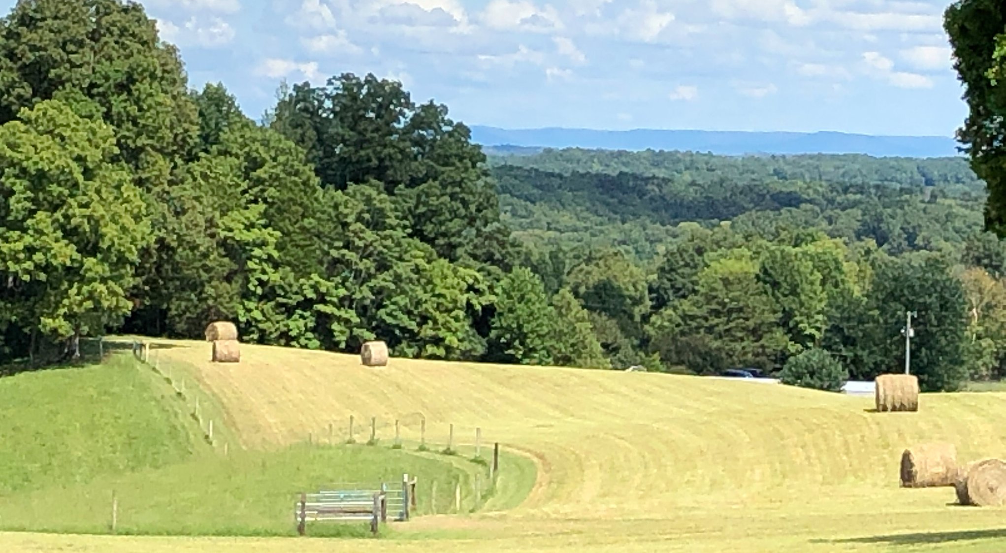Freshly cut hay field with bales, fence gate and distant mountains